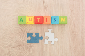 top view of autism lettering made of multicolored cubes near puzzle parts on wooden table