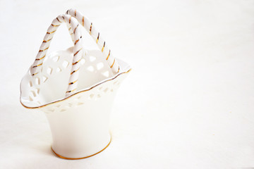 White porcelain basket with handles with gold interlacing on a white background, closeup. Decorative white vase with gold rim, with copy space for text. Gift idea, empty basket, porcelain tableware.