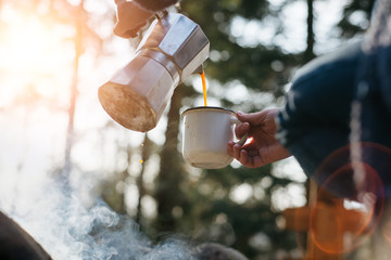 Horizontal outdoors image of young woman pours itself hot beverage in mountains near to bonfire ....