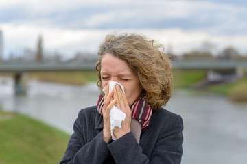 Woman blowing her nose on a tissue outdoors