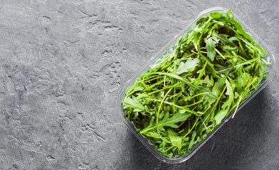 Fresh green arugula leaves in a plastic package box on Dark grey black slate background with copy space. top view