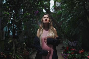 Portrait of a young beautiful pregnant woman with long hair in a long romantic pink dress in a tropical forest