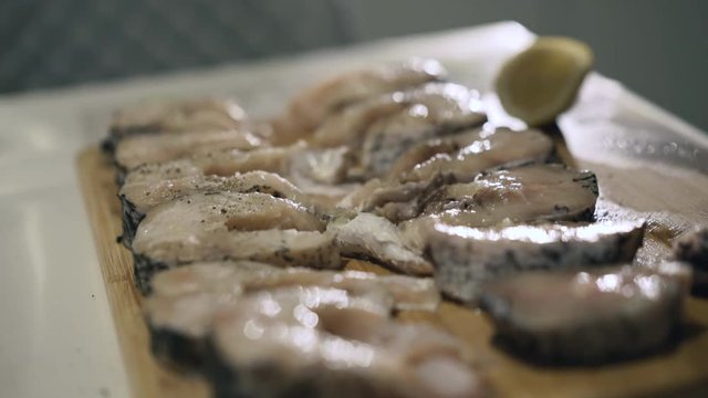 Female hands strewing spices on fish fillet on wooden tablet. Close up