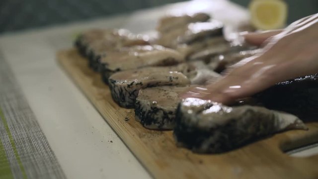 Female hands strewing spices on fish fillet on wooden tablet. 4K