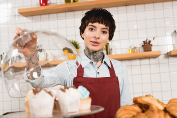 selective focus of beautiful barista standing near delicious desserts and looking at camera