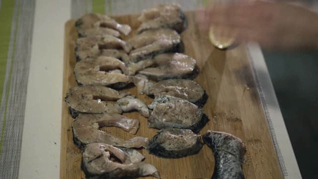 Female hands strewing spices on fish fillet on wooden tablet. 4K