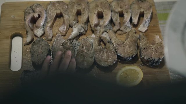 Female hands strewing spices on fish fillet on wooden tablet. 4K