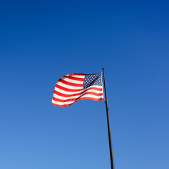 Square image of national flag of the United States of America, also called Stars and Stripes, Old Glory or Star-Spangled Banner waving on July 4th in the wind and sunlight against clear blue sky