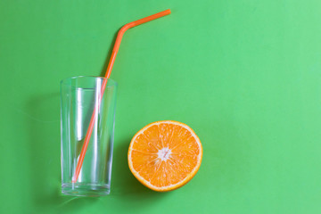 A glass cup with a straw and an orange on a green background.