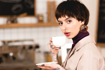 pretty businesswoman drinking coffee and looking at camera in coffee shop