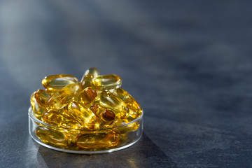 Fish oil capsules with omega 3 and vitamin D in petri box ove a grey background