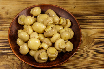 Ceramic plate with pickled champignons. Marinated mushrooms on wooden table