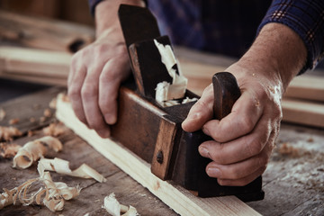 Hands of a carpenter using a vintage plane