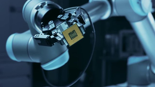 Modern High Tech Authentic Robot Arm Holding Contemporary Super Computer Processor Smoothly Moving into Focus. Industrial Robotic Manipulator End Effector Holding CPU Chip Moves Towards Camera Focus