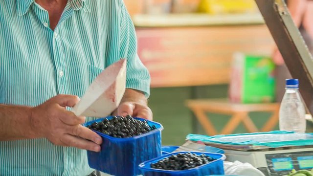A man who is selling blueberries is weighing each of the small plastic baskets separately so that the weight in all of them is the same.