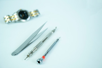Various small metal watch repair tools place in front of gold/stainless metal strap analog watch on white background.