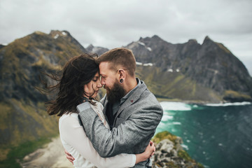 Naklejka premium Wedding couple travelers on a hill in Norway, Kvalvika. Beautiful view of the beach, Lofoten, Norway.