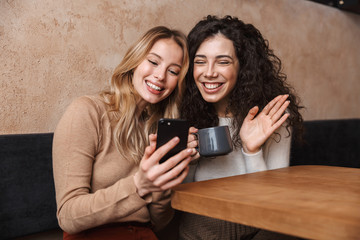 Emotional shocked girls friends sitting in cafe using mobile phone.