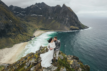 Wedding couple travelers on a hill in Norway, Kvalvika. Beautiful view of the beach, Lofoten, Norway.