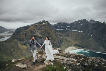 Wedding couple travelers on a hill in Norway, Kvalvika. Beautiful view of the beach, Lofoten, Norway.