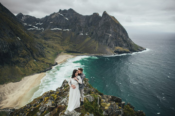 Fototapeta na wymiar Wedding couple travelers on a hill in Norway, Kvalvika. Beautiful view of the beach, Lofoten, Norway.