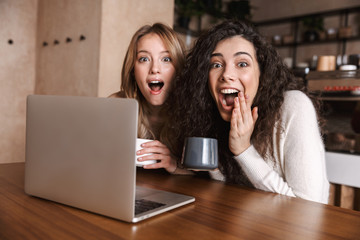 Emotional shocked girls friends sitting in cafe using laptop computer.