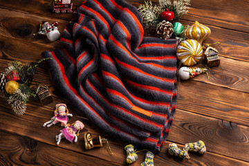 knitted scarf in black and red stripes and christmas decorations on a wooden background