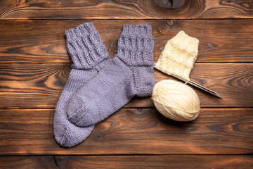 Fototapeta na wymiar gray knitted socks and a ball of white thread with knitting needles on a wooden background