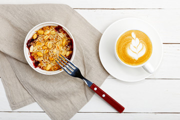 Homemade crumble with blackberries, peanuts and sesame and cup of coffee cappuccino on white wooden table. Top view.
