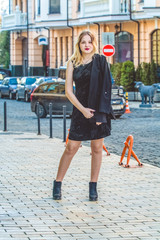 The young girl in black clothes in spring sunny day walks on old city streets. Dress, jacket and coat. Modern fashion.