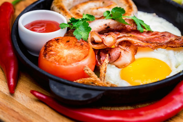 Nutritious meal with fried egg, sausage, bacon, tomato and sauce in frying pan