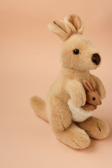 Soft toy mom kangaroo with a baby is located on a peach background, vertical