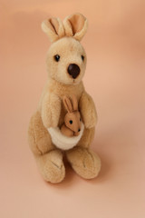 Soft toy mom kangaroo with a baby is located on a peach background, vertical