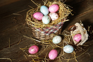 Colorful Easter eggs in a basket decorated with straw on a wooden rustic background