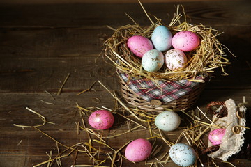 Colorful Easter eggs in a basket decorated with straw on a wooden rustic background with copy space for text