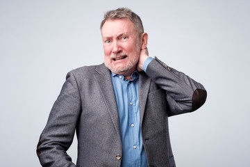 Frustrated senior man in suit holding hand on his neck