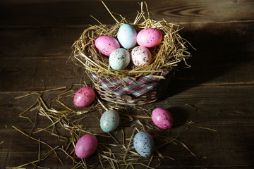 Easter eggs in a straw decorated basket on a wooden rustic background