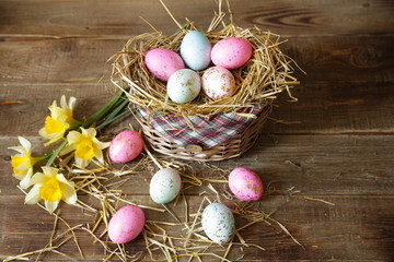 Easter eggs in a basket decorated with straw and narcissus on a wooden rustic background with copy space for text.Flat lay. Post card. Easter background.