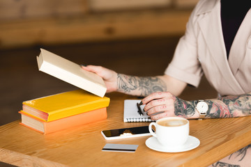 partial view of businesswoman sitting at table with books, smartphone and coffee cup
