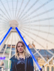 The young girl in black clothes walks around the city near sights. Ferris wheel. Amusement park. Happy smile.