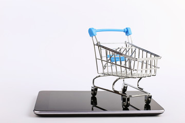 Shopping cart stands on the smartphone. Online sales concept.