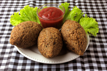kibbeh fried with tomato sauce on a plate, on table lined with checkered tablecloth