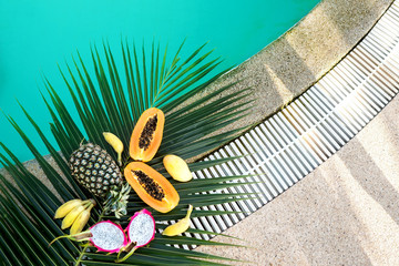 tropical fruits lie on palm leaves near the pool