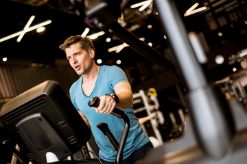Fototapeta na wymiar Man doing exercise on elliptical cross trainer in sport fitness gym club