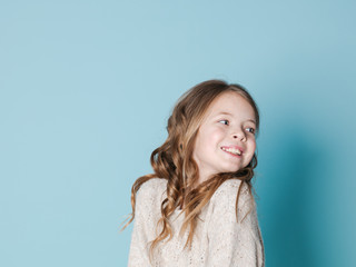 pretty and cool 9 year old girl with brown wool sweater posing in front of blue background