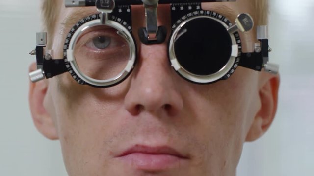 Tilt up shot with extreme close up of young man wearing trial frame looking at camera, then smiling as unrecognizable optometrist changing lenses