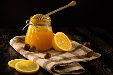 Honey with nuts, lemon and a spoon for honey on a checked tablecloth with black background