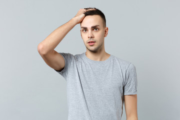 Fototapeta premium Portrait of shocked handsome young man in casual clothes looking camera putting hand on head isolated on grey wall background in studio. People sincere emotions, lifestyle concept. Mock up copy space.