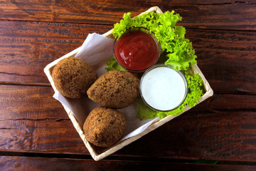Fried kibbeh with tomato sauce in a basket, over rustic wooden table