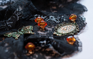 selective focus of decorative green butterfly, orange beads, frame and rhinestones on black lace on white